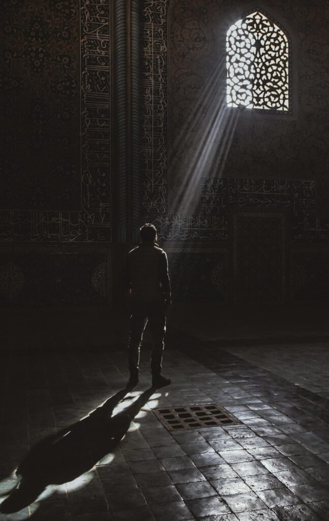 Solitary figure illuminated by light in a dark interior, symbolizing reflection and inner clarity